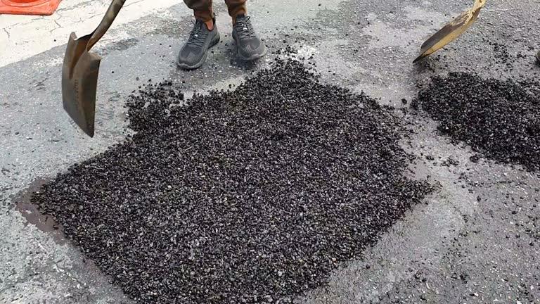 Worker filling pothole with asphalt patch on road